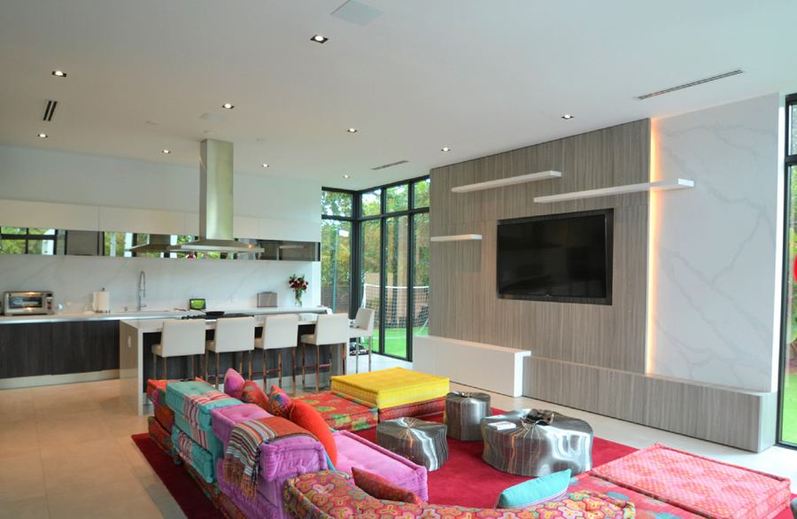 Open living room with a wood-grain TV wall, floating shelves and kitchen behind
